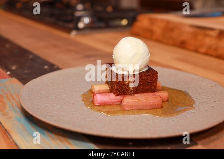 A plate of traditional parkin with Yorkshire rhubarb and ice cream on a wooden kitchen table Stock Photo