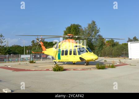 A bright yellow and orange rescue helicopter parked on a concrete helipad surrounded by trees and fencing. The aircraft is ready for emergency operati Stock Photo