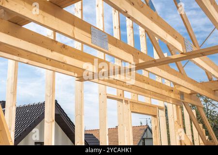 Workers are building the framework of a house, showcasing the wooden beams and trusses against a blue sky in a neighborhood setting. Stock Photo