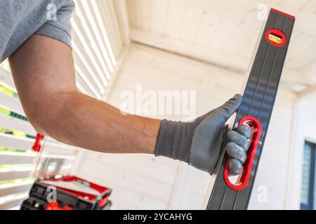 A worker in a gray shirt and gloves holds a leveling tool, focusing on achieving accuracy in a bright, modern space. Tools are nearby, ready for the n Stock Photo