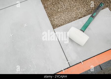 Workers are installing gray flooring outdoor patio tiles using a rubber mallet to ensure a tight fit. The setting is a construction site in the aftern Stock Photo