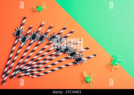 Drinking straws with spiders for Halloween celebration on orange and green background. Top view, flat lay. Stock Photo
