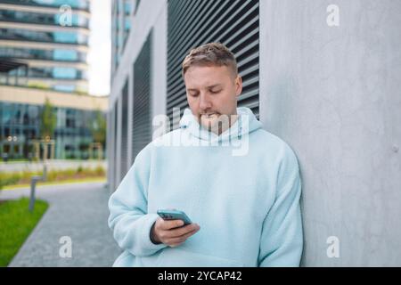 Successful young Caucasian man walking outside office building, engineer software developer programmer smiling and happy using test app on phone  Stock Photo