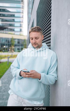 Successful young Caucasian man walking outside office building, engineer software developer programmer smiling and happy using test app on phone  Stock Photo