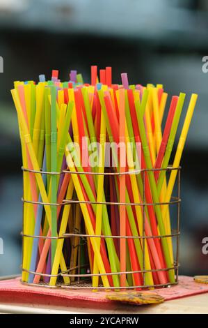 Multi-colored, plastic, disposable drinking straws with bellows standing upright in a wire container. Stock Photo