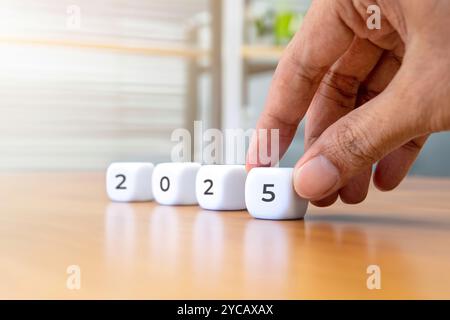 Closeup image of hand arrange a white cube with the number 2025. New year concept. Stock Photo