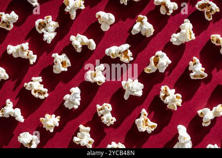 Classic buttery popcorn scattered across a vibrant red background evokes memories of retro movie nights and timeless snacking. Stock Photo