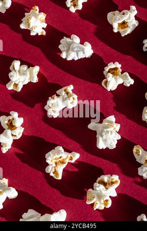 A playful, nostalgia-inducing pattern of popped popcorn scattered on a rich red background, evoking memories of classic movie nights. Stock Photo