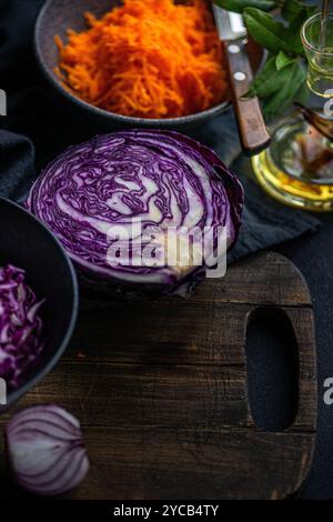A thematic display of fresh salad ingredients with sliced red onion, red cabbage, shredded carrots and olive oil arranged on a rustic wooden board, em Stock Photo