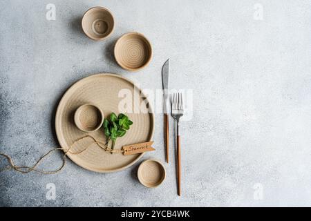 From above, a serene shamrock-themed table setting on a textured grey surface, featuring ceramic plates, wooden utensils, and a small plant tied with Stock Photo