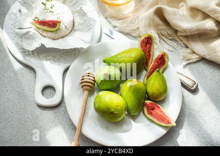Top view of green whole figs and sliced ripe figs with a wedge of Brie cheese, honey dipper on a marble board. Soft natural lighting enhances the fres Stock Photo