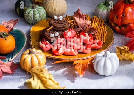 Colorful Halloween-themed treats arrangement featuring cookies with marshmallow toppings, gummy fangs, pretzel sticks, persimmons, and decorative pump Stock Photo