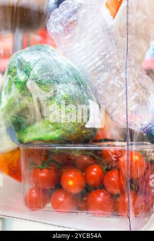 Broccoli and cherry tomatoes sealed in plastic, highlighting food packaging, waste, and sustainability concerns. Stock Photo