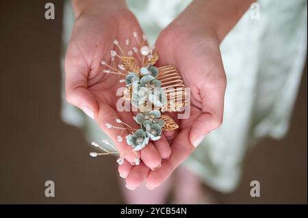 A close-up image showing a bride holding a delicate floral hair accessory with gold accents and subtle hues, symbolizing the elegant details of a wedd Stock Photo