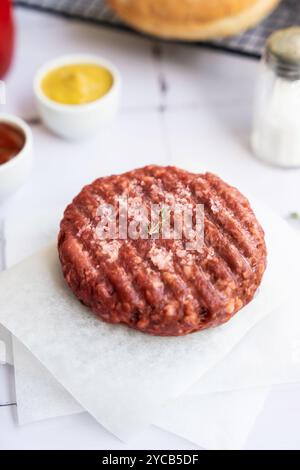 Close-up view of a beef burger patty, garnished with a sprig of thyme, presented on a square of wax paper Condiments and a checkered napkin in the bac Stock Photo