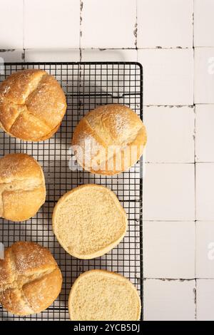 Overhead shot of freshly baked round bread loaves, some sliced, placed on a cooling rack over a cracked white tile surface Stock Photo