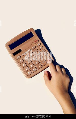 A close-up image of a hand pushing a button on a metallic brown calculator against a neutral background, emphasizing simplicity and productivity Stock Photo
