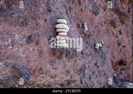 Stacked pebbles carefully balanced on the rugged red rock wall of Vereda da Ponta de São Lourenço Stock Photo