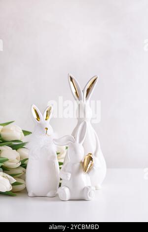 Three Easter rabbits figurines with bouquet of white tulips on white background. Easter celebration concept. Copy space. Front view Stock Photo
