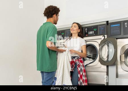 Couple interacting at a laundromat while doing laundry together in the afternoon Stock Photo