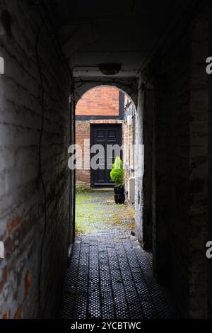 View through a dark passageway to a courtyard with a black door Stock Photo