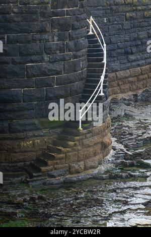 Curved white metal hand railing leading steps to rocky beach with tide out at Aberystwyth Stock Photo