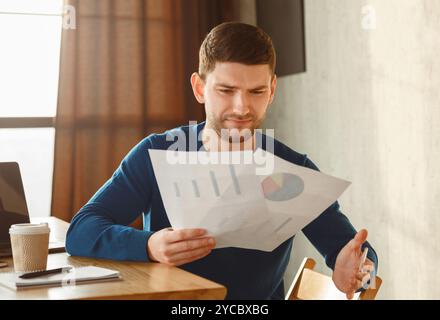 Discontented Office Worker Looking At Documents Sitting In Modern Office Stock Photo