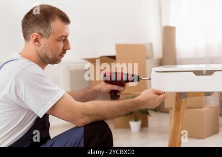 Side-View Of Carpenter Man Assembling Table Using Electric Drill Indoors Stock Photo