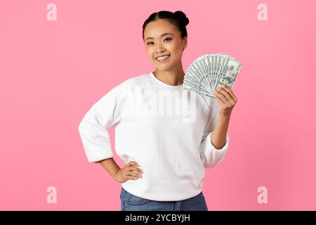Young woman smiles while holding cash against a pink background Stock Photo