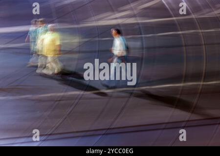Artistic long-exposure photograph capturing the dynamic motion of people walking in the city at night. The image presents a blur effect conveying move Stock Photo