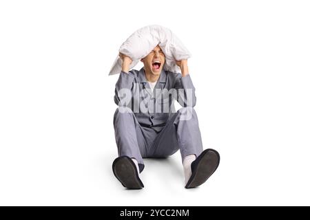 Angry young man in pajamas screaming and holding pillow over head isolated on white background Stock Photo