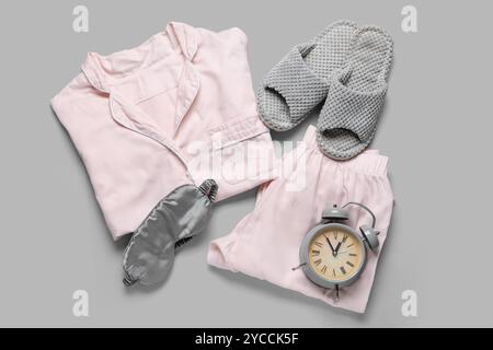 Pink pajamas with slippers, sleeping mask and alarm clock on light background Stock Photo