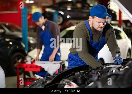 Professional mechanic man in uniform repairing car in auto repair garage Stock Photo