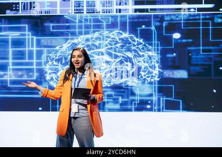 Upbeat programmer using tablet during presentation, exploring ways emerging AI technologies can enhance businesses. Jolly woman at event presents artificial intelligence using device and microphone Stock Photo