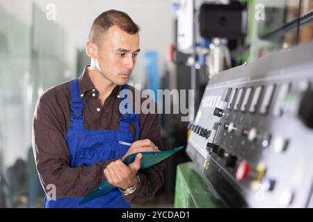 Technician writing on clipboard while operating industrial machinery Stock Photo