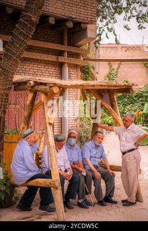 KASHGAR, XINJIANG CHINA - July 20, 2022: Five elderly men of the Uyghur minority having a conversation at a street in Kashgar Old Town. Chinese flags Stock Photo