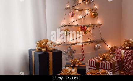 A tree-shaped Christmas decoration hangs on a white wall, with several gift boxes in front.3d rendering Stock Photo