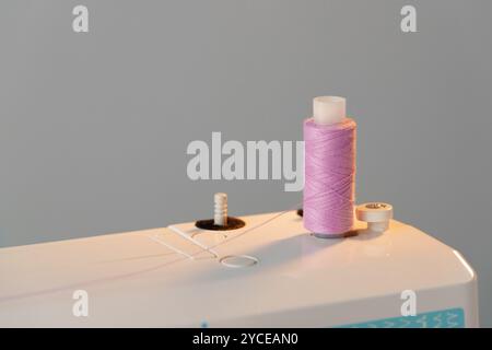 View of a sewing machine with a spool of pink thread placed on top Stock Photo