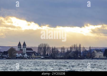 Evening view of a village with the church of St. Peter and Paul on Reichenau am See, illuminated by the setting sun, in the cloudy sky, harbour, Allen Stock Photo