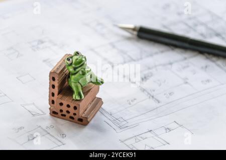 Toy frog sitting on a brick on architect sketches background Stock Photo