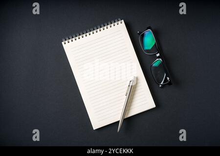 Top view of notebook, glasses and ballpoint pen on dark grey background Stock Photo