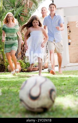 Happy family playing soccer and running towards the camera in the backyard of their home Stock Photo