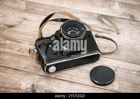 Black Soviet film camera in a leather case on a wooden unpainted surface with knots. Stock Photo