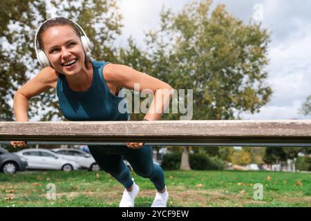 Smiling woman performing push-ups on a bench during outdoor workout. Stock Photo