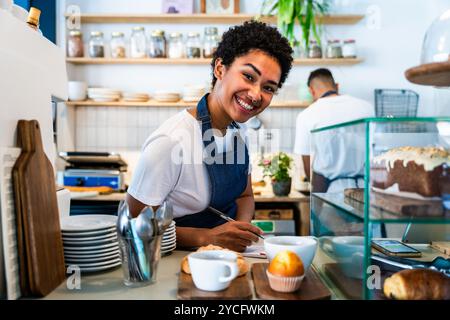 Bakery, happy portrait of hispanic black man and woman in cafe ready for serving pastry, coffee and baked foods - Confident waiter barista by counter Stock Photo