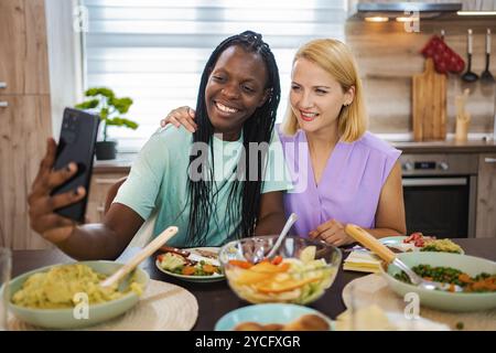 Friends enjoying a joyful meal and taking selfies together Stock Photo