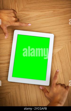 Person, hands and tablet with green screen for advertising, marketing or software app above on wooden table. Top view, developer and closeup with Stock Photo