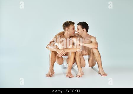 Two young men sit closely together, exchanging loving gazes in a light filled space. Stock Photo