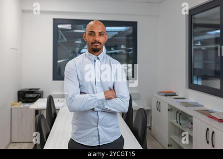 Confident young African American man, proudly posing at an office with crossed arms, portrait shot. Professionalism and expertise in business concepts Stock Photo