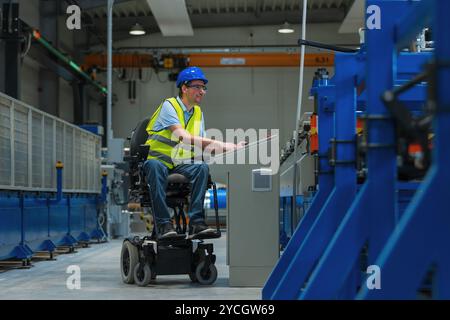 Man with disability in yellow vest, engineer in a factory unit checking a work process. inclusion and diversity concepts. Stock Photo